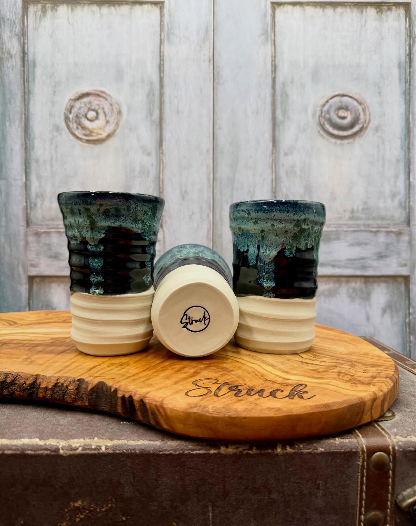 Handcrafted ceramic cups with a unique glaze finish, displayed on a wooden serving board engraved with the word "Struck." The cups feature a textured design in shades of blue and green, showcasing artisanal craftsmanship. Ideal for serving beverages or as decorative pieces in modern home decor.